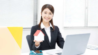 女性が家のプラモデルを持ってデスクに座っている